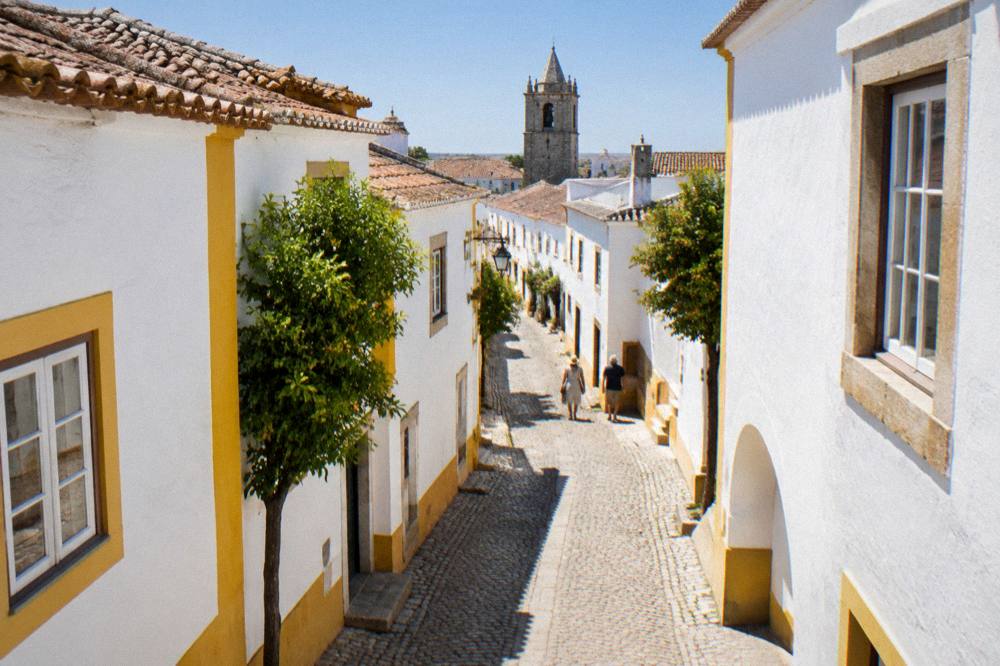 A narrow cobbled street in Évora with whitewashed houses, yellow trim and strong summer shadows