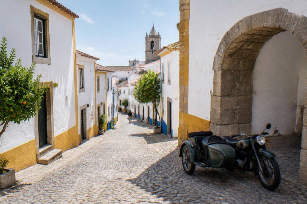 A vintage motorcycle with a sidecar parked on a cobbled street beside a stone archway