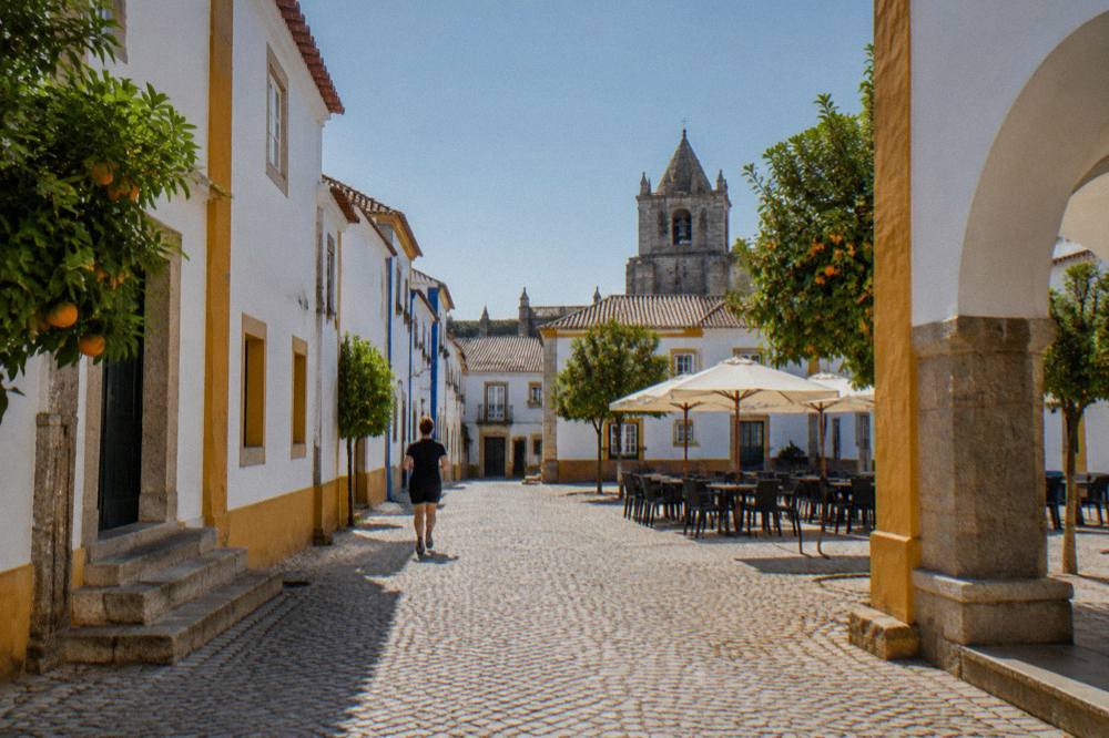 A restaurant terrace in an Évora square at dusk with warm lighting and empty chairs