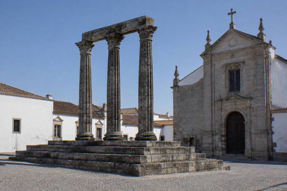 Granite Roman temple with columns standing beside a church in Évora's old town
