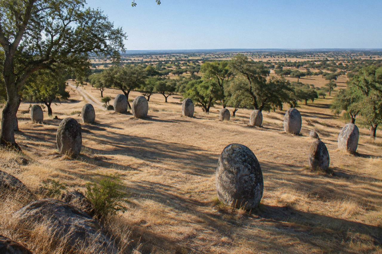 Standing stones of the Almendres cromlech rising from open grassland under a wide Alentejo sky