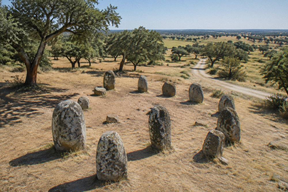 A gravel track leading through cork oak and open fields toward the Almendres stone circle