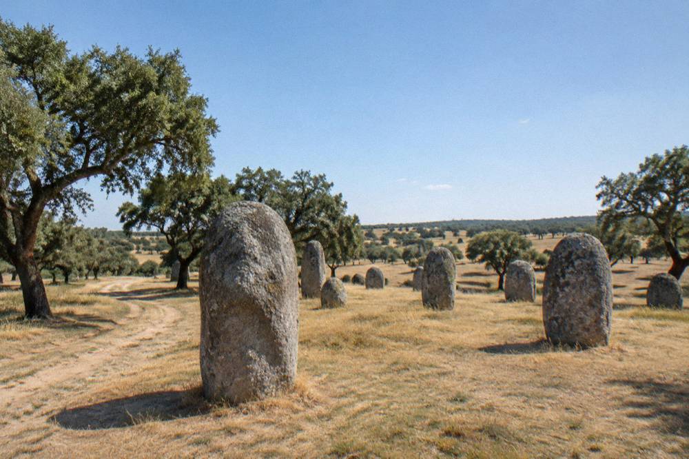 A weathered standing stone at the Almendres cromlech with rolling Alentejo pasture behind it