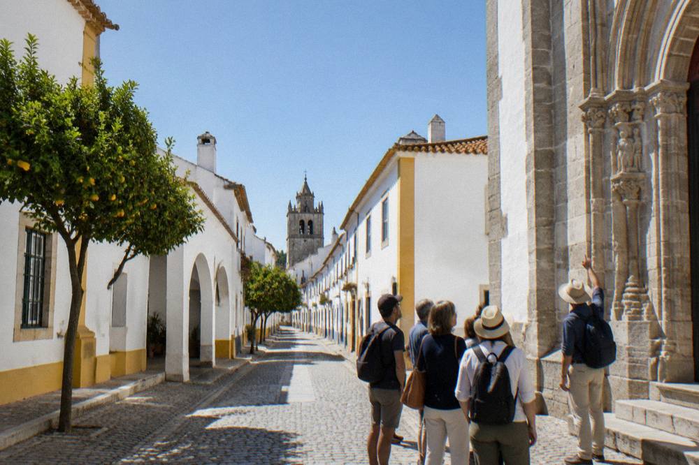 Guide pointing out carved stone details on a church facade to a small walking group in Évora
