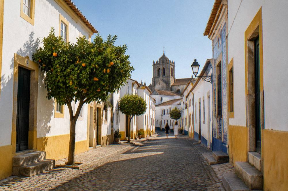 Sunlit lane of white houses with yellow trim and blue tiles inside the walls of Évora