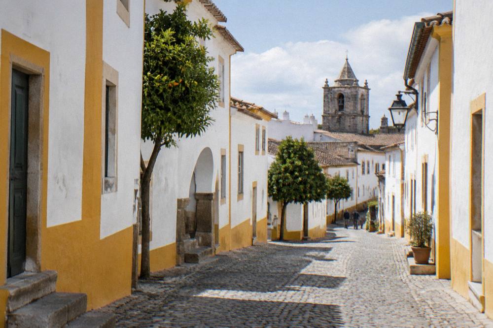 A quiet cobbled street of whitewashed houses with yellow trim inside the walls of Évora
