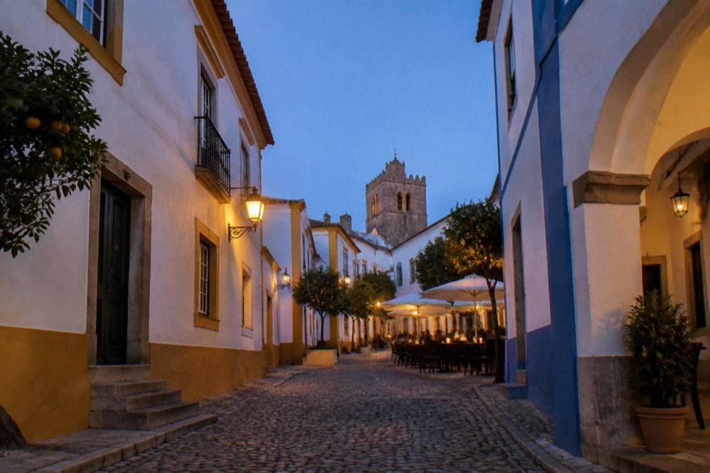 Tables set for the evening outside restaurants on a lit square in Évora