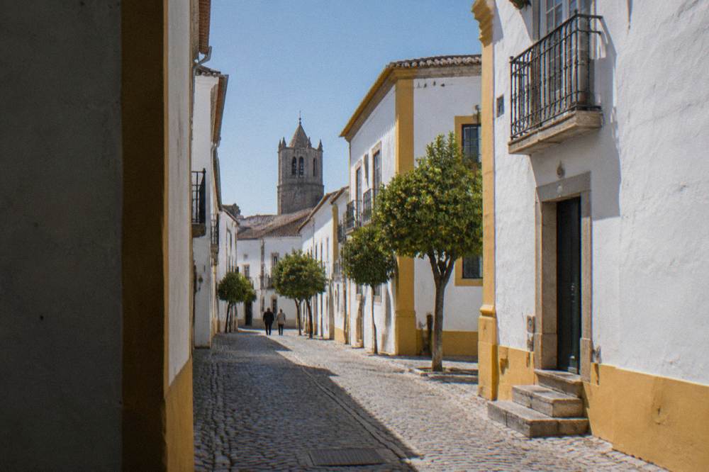 A quiet cobbled street in Évora lined with white houses and iron balconies