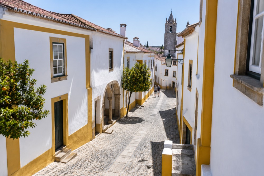 A narrow street in Évora with white walls, yellow trim and stone paving