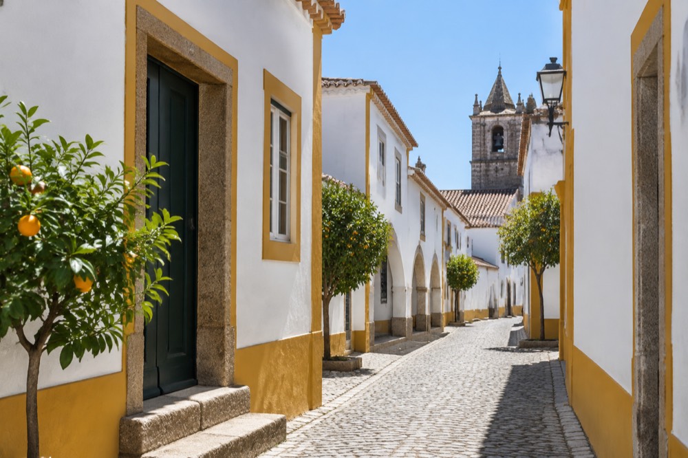 Sunlit narrow street with white walls and yellow trim inside the walled centre of Évora