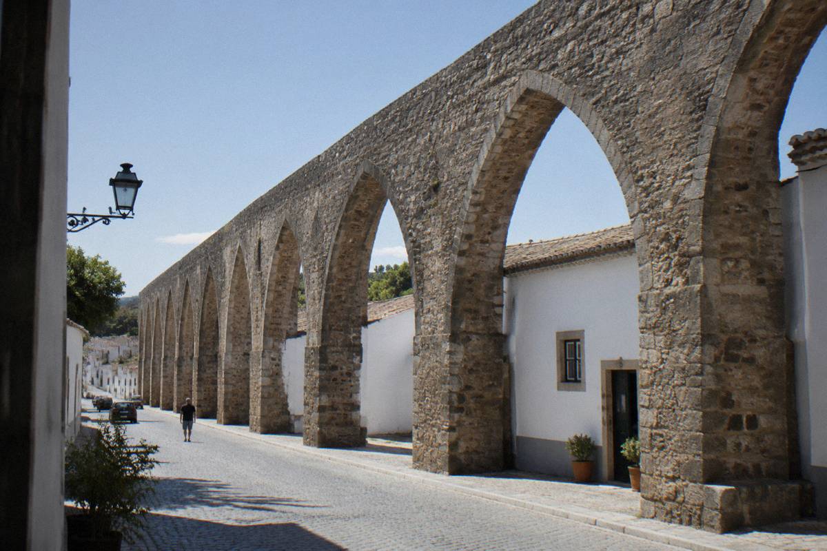 A very long raised stone aqueduct of pointed arches crossing a street of small whitewashed houses