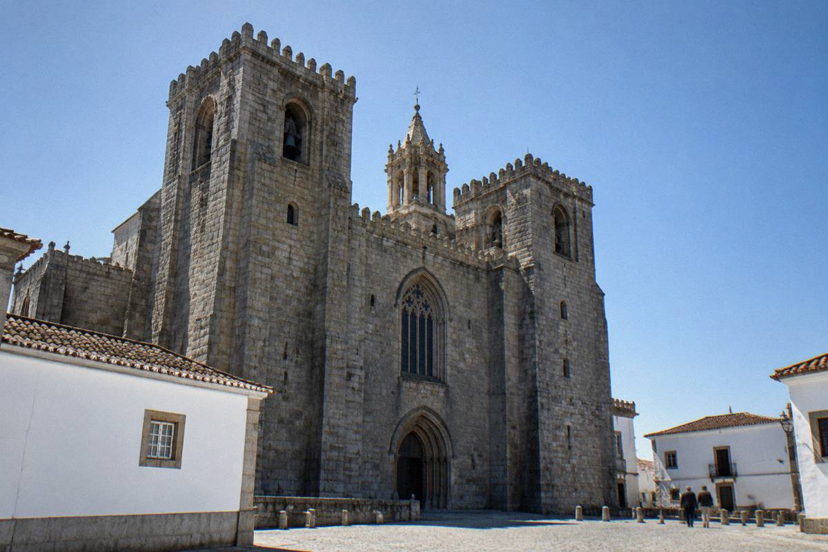 A heavy granite cathedral with two crenellated towers and a scaled stone lantern rising over whitewashed rooftops