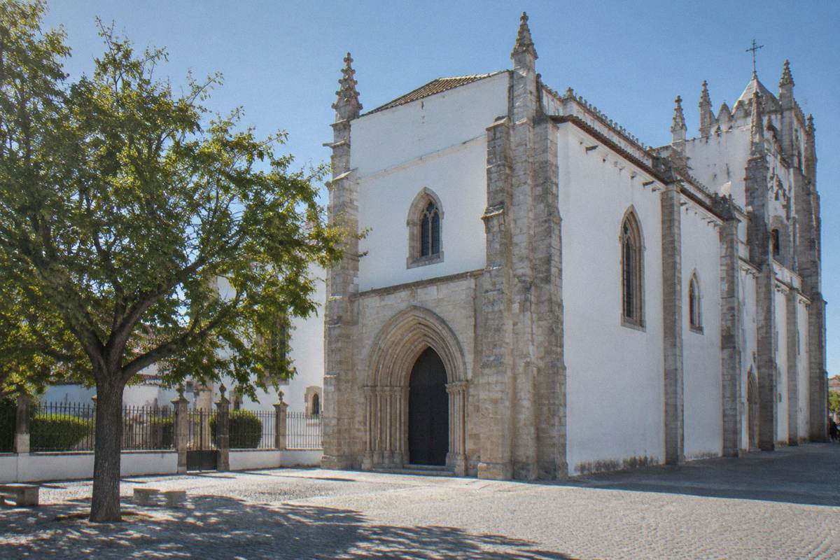 A large late-Gothic church of whitewashed walls and pale granite with a plain arched portal, seen from outside in clear light