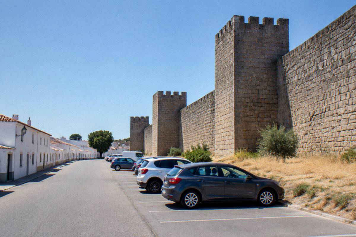 A quiet street of low whitewashed houses beside a long granite town wall with dry grass at its foot