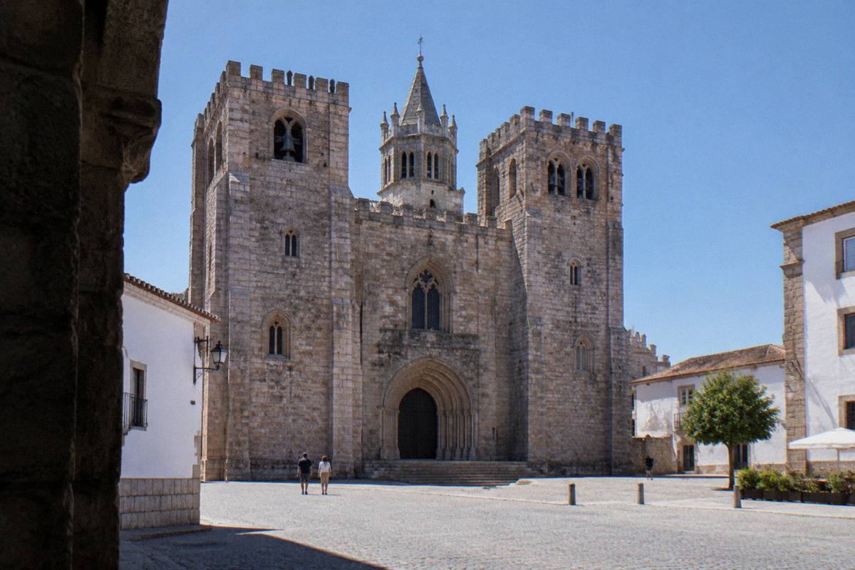 Late morning below a massive granite cathedral front with two crenellated towers on a small paved square