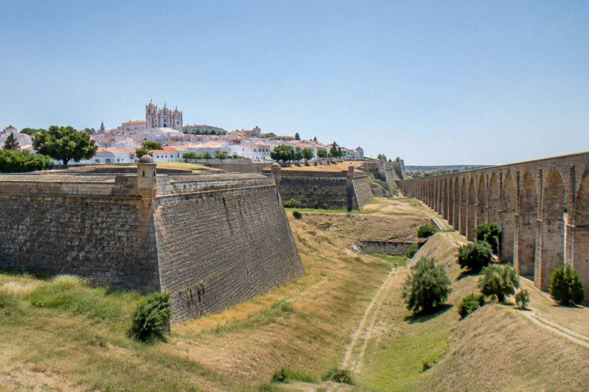 Enormous angular granite bastion walls around a hilltop town with a long tall arched aqueduct beside it