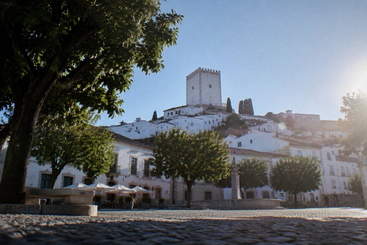 A hillside old town of whitewashed and pale marble houses below a tall square white castle keep