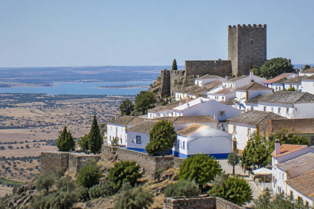 A walled hilltop village of whitewashed houses trimmed in blue below a stout castle tower above a dry plain