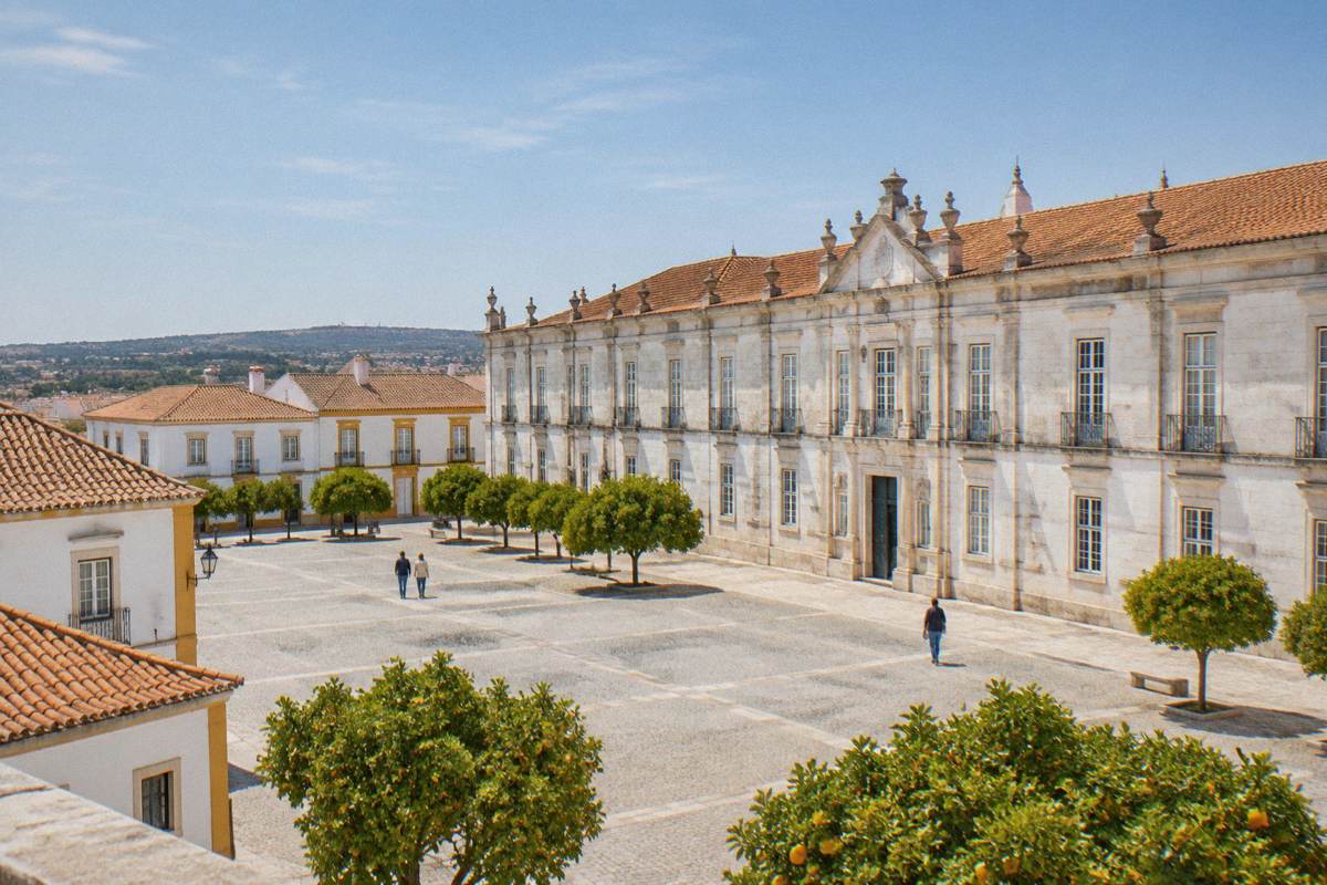 A broad sunlit square before a long pale marble palace front with orange trees and whitewashed houses