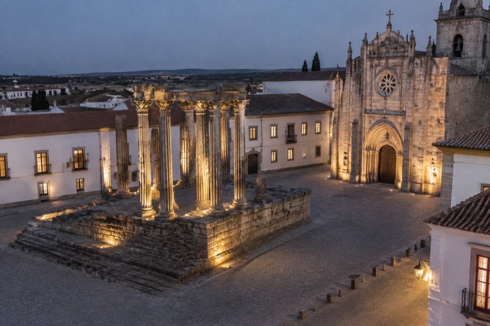 Floodlit Roman temple columns beside the cathedral in Évora at night