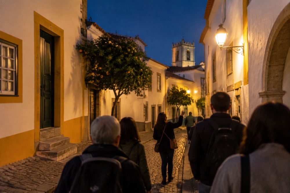A guide leading a small group of visitors through a lit street in Évora at night