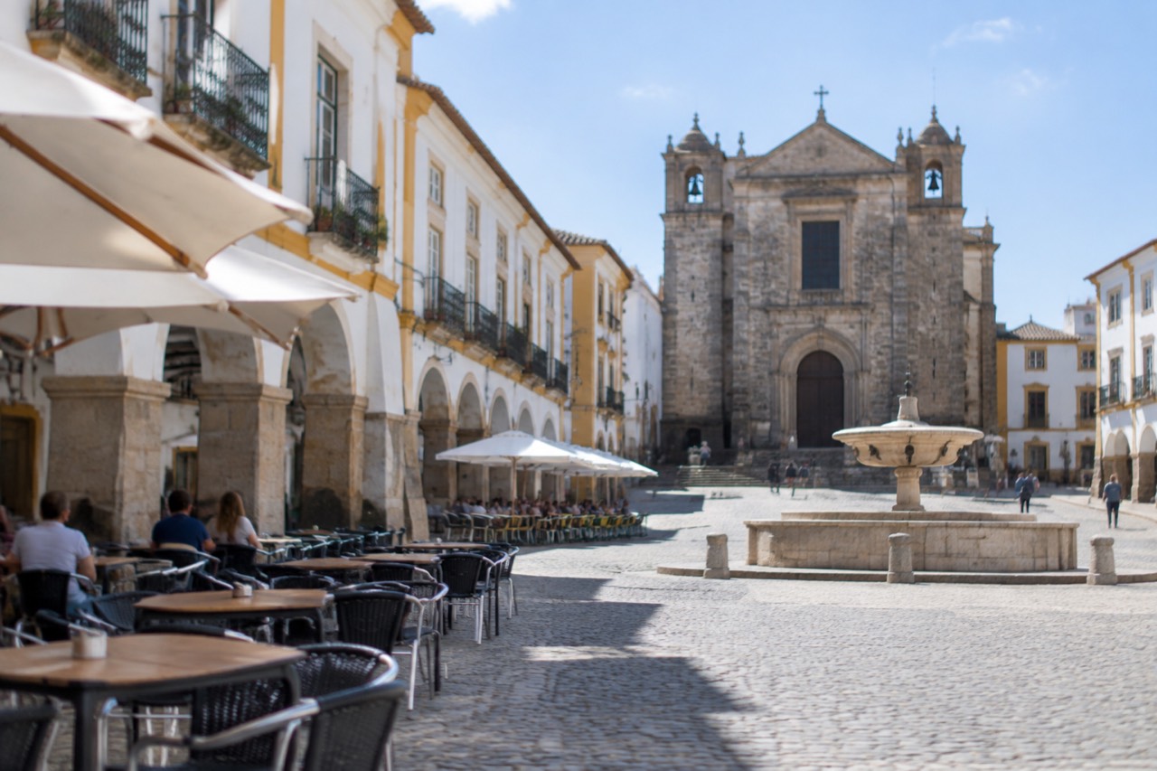 The arcade of Praça do Giraldo in Évora on a bright morning with café tables along the white buildings