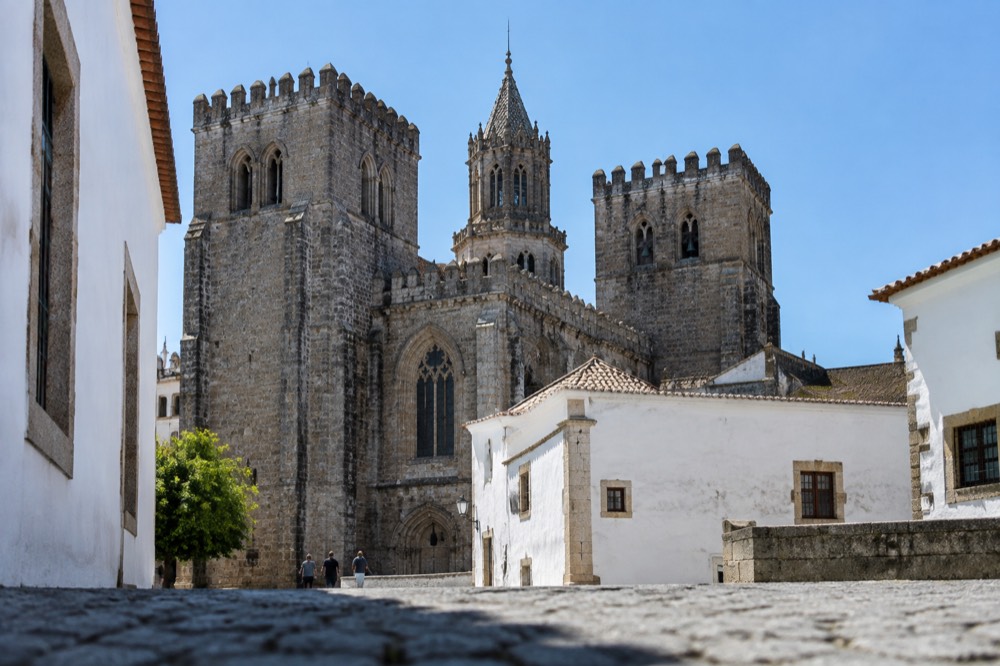 The Gothic cathedral of Évora seen from a narrow street with towers against the sky