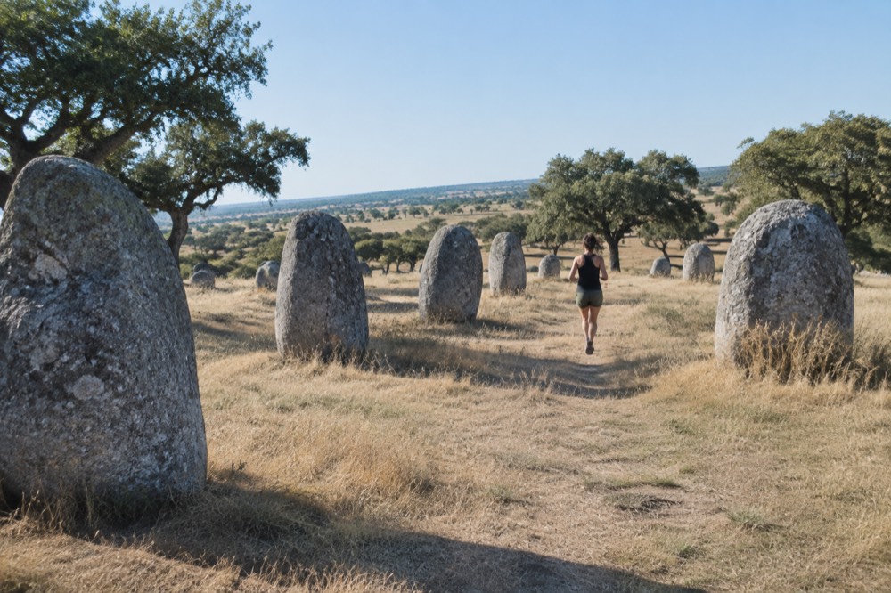 Standing stones of the Almendres Cromlech on a grassy hillside under a wide sky