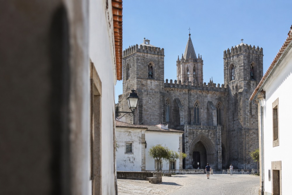 The Gothic cathedral of Évora seen from a narrow lane with a blue sky